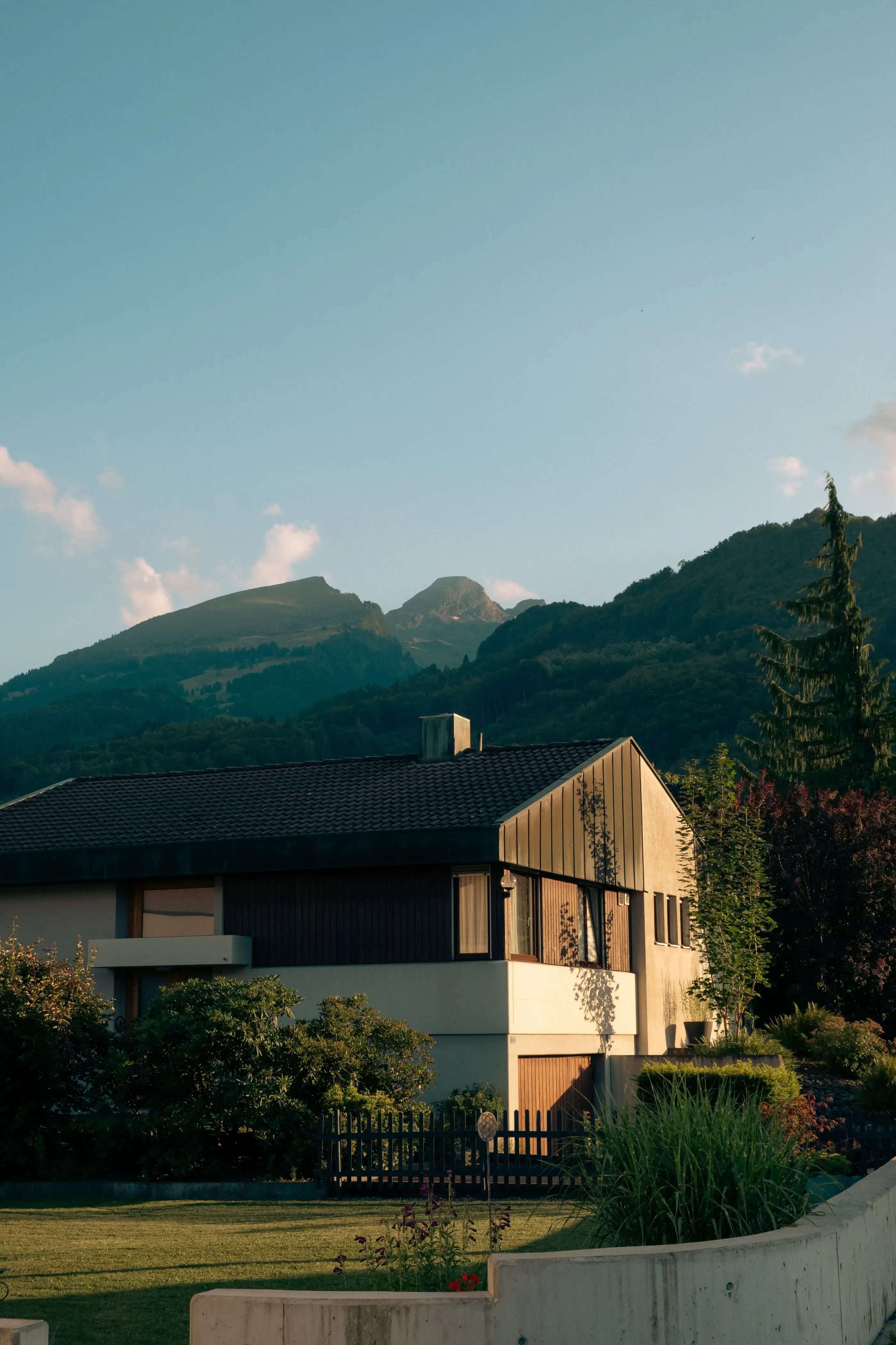 Maison individuelle crépie avec bardage bois, montagnes en arrière-plan